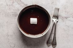 a bowl with chocolate and marshmallows in it next to two forks on a table