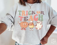 a woman wearing a trick or teach sweatshirt with her hands in her pockets and the words trick or teach on it