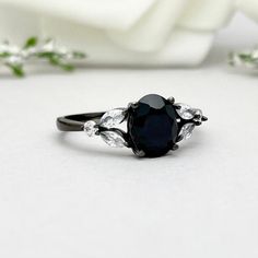 a black diamond ring sitting on top of a white table next to a bouquet of flowers