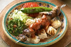 a plate with skewered meat and veggies on it sitting on a table