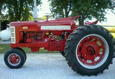 an old red tractor is parked on the side of the road