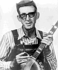 an old photo of a man with glasses holding a guitar and looking at the camera