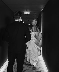 a man and woman walking down a hallway together in black and white photo with light coming through the doorway