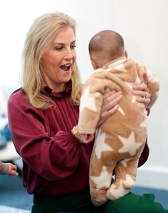 a woman holding a stuffed animal in her hands while sitting on the floor next to a baby