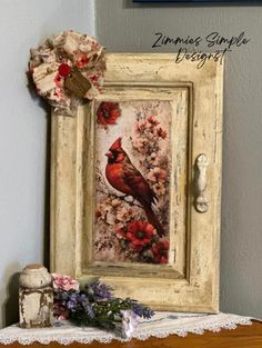 a red bird sitting on top of a wooden table next to a white framed painting