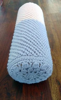 a crocheted blue and white blanket laying on top of a wooden floor next to a glass vase