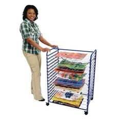 a woman standing next to a metal rack with books on it and holding the top shelf