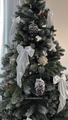 a decorated christmas tree with white bows and pine cones