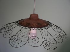 a lamp hanging from the ceiling with an intricate design on it's side and a pink light bulb in the middle