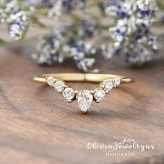 a gold ring with three pear shaped diamonds on it and blue flowers in the background