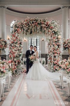 a bride and groom standing in front of a floral arch