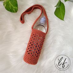 an orange crocheted water bottle bag sitting on top of a white fur covered floor