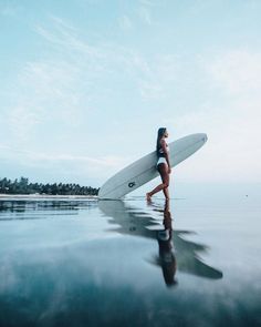 a woman walking in the water with a surfboard