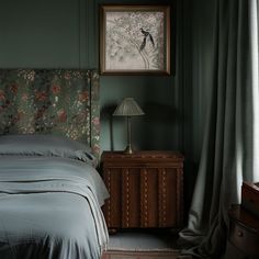 a bed sitting next to a window in a room with curtains on both sides and a painting above it