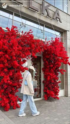 a woman walking past a building with red flowers