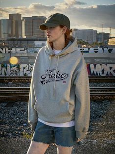 a woman standing in front of train tracks wearing a grey hoodie with the word fluke on it