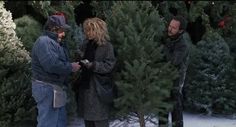 two men and a woman standing in front of a christmas tree stand talking to each other