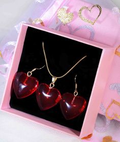 three red heart shaped glass pendants in a pink box with gold chain necklace and earring