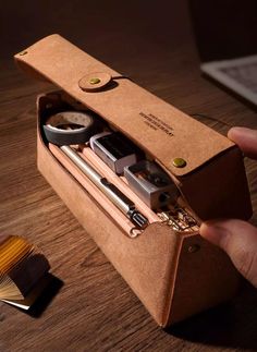 a person is holding a brown case with some items in it on a wooden table