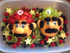 two decorated fruits in the shape of faces with eyes and nose, surrounded by berries and kiwis