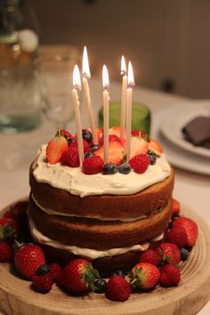 a cake with strawberries and blueberries on it is sitting on a wooden plate