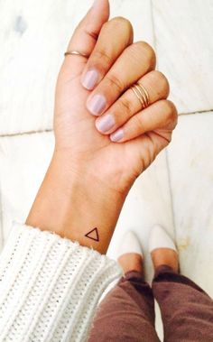 a woman's hand with a small triangle tattoo on it, while she is holding her wrist