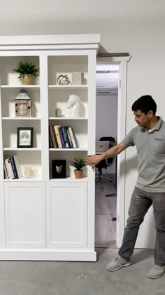 a man standing in front of a white book shelf with books on top of it