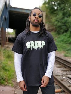 Halloween collection by Boisterous London, handmade here in the U.K. Each t-shirt is hand printed. Features contrast glow in the dark creep logo, short sleeves, round ribbed neckline, comes in a unisex loose fit unisex. Sleeves have been rolled up for styling purposes only.  SIZING AND CARE  Model height 5ft 11 model is a size large. Model is wearing a size XL. Please check exact chest measurements for desired size. XS 34/36" S 36/38" M 38/40" L 41/42" XL 43/44" 2XL 45/47"  DOMESTIC SHIPPING  Al Spooky Short Sleeve Tops For Streetwear, Horror Themed Letter Print Crew Neck T-shirt, Halloween Graphic Tee For Streetwear, Spooky Letter Print T-shirt For Streetwear, Hip Hop Halloween T-shirt For Streetwear, Horror Crew Neck Tops For Streetwear, Black Cotton Top With Glow In The Dark Details, Short Sleeve T-shirt For Halloween Streetwear, Grunge Halloween T-shirt For Streetwear