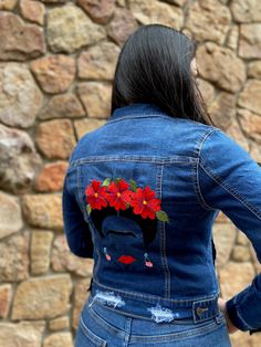 a woman wearing a jean jacket with red flowers on it's lap and back