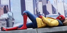 a spider man doll laying on top of a ledge in front of a cityscape