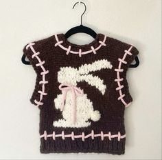 a knitted sweater hanging from a hook on a wall with the number seven in pink and white