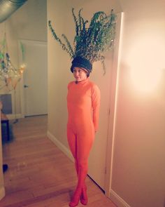 a woman in an orange jumpsuit and hat with plants on her head