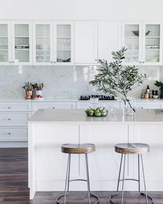 two stools sit at the center of a kitchen island with marble countertops and white cabinets