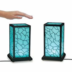 a hand is reaching for two small lamps on the ground, one blue and one black