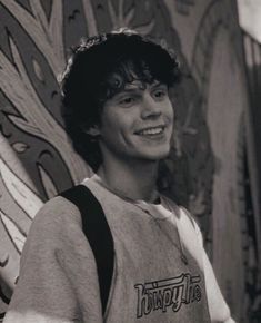 a young man standing in front of a wall with graffiti on it's walls