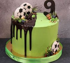 a green cake with soccer balls on top and chocolate drizzle dripping down the side