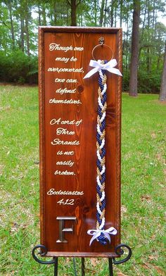 a wooden plaque with white and blue ribbons attached to it's sides in the grass