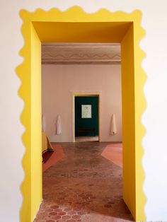 an open doorway in a room with yellow walls and red bricks on the floor, leading to a green door