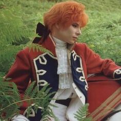 a man with red hair sitting on the ground in front of ferns and fern leaves