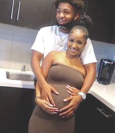 two people standing in a kitchen with one holding the other's pregnant baby bump