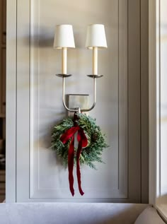 a christmas wreath hanging on the wall next to two lights with red ribbon and white lampshades