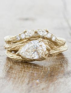 a gold ring with two pear shaped diamonds on it, sitting on top of a piece of wood