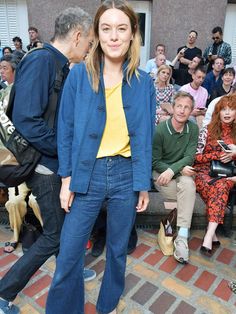 a woman standing in front of a crowd wearing blue jeans and a yellow t - shirt