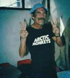 a man in a black shirt is making the peace sign with his hands and wearing a blue hat