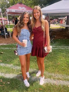 two young women standing next to each other on a grass covered field with tents in the background