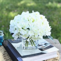 a vase with white flowers sitting on top of a wooden table next to a book