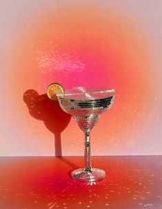 a martini glass with a slice of lemon in it on a red and pink background