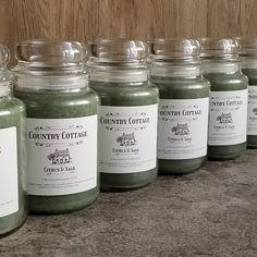 six jars of green stuff sitting on top of a counter