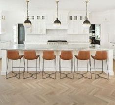 a large kitchen with white cabinets and wooden flooring, along with bar stools