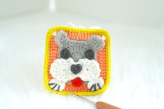 a crocheted square with a raccoon on it next to a knitting needle